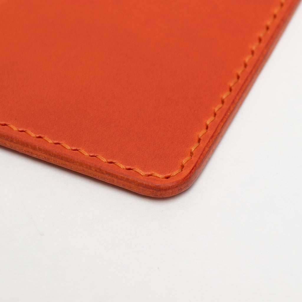 Close-up of an orange leather passport holder with visible stitching on a white background