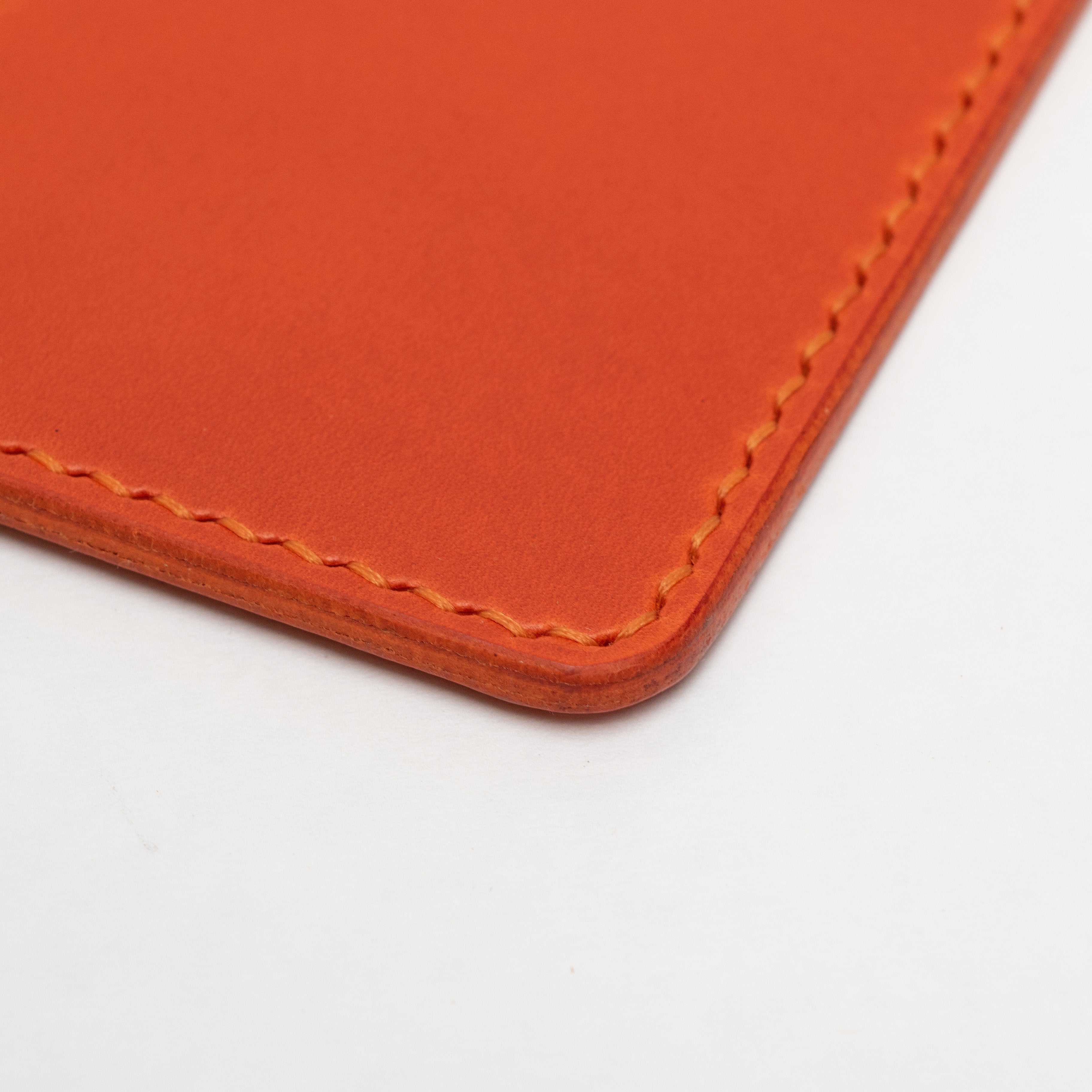 Close-up of an orange leather passport holder with visible stitching on a white background
