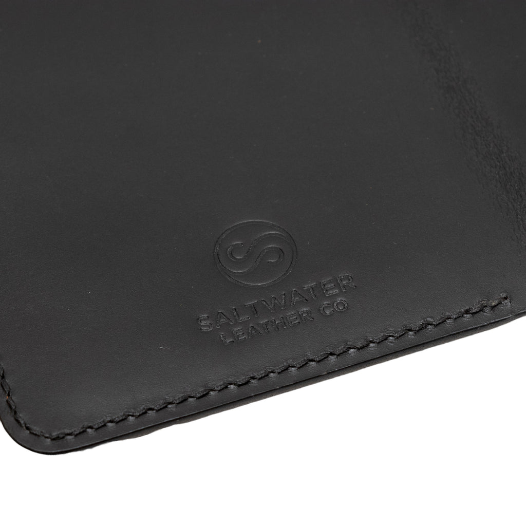 Close-up of a black leather passport holder with Saltwater Leather branding.