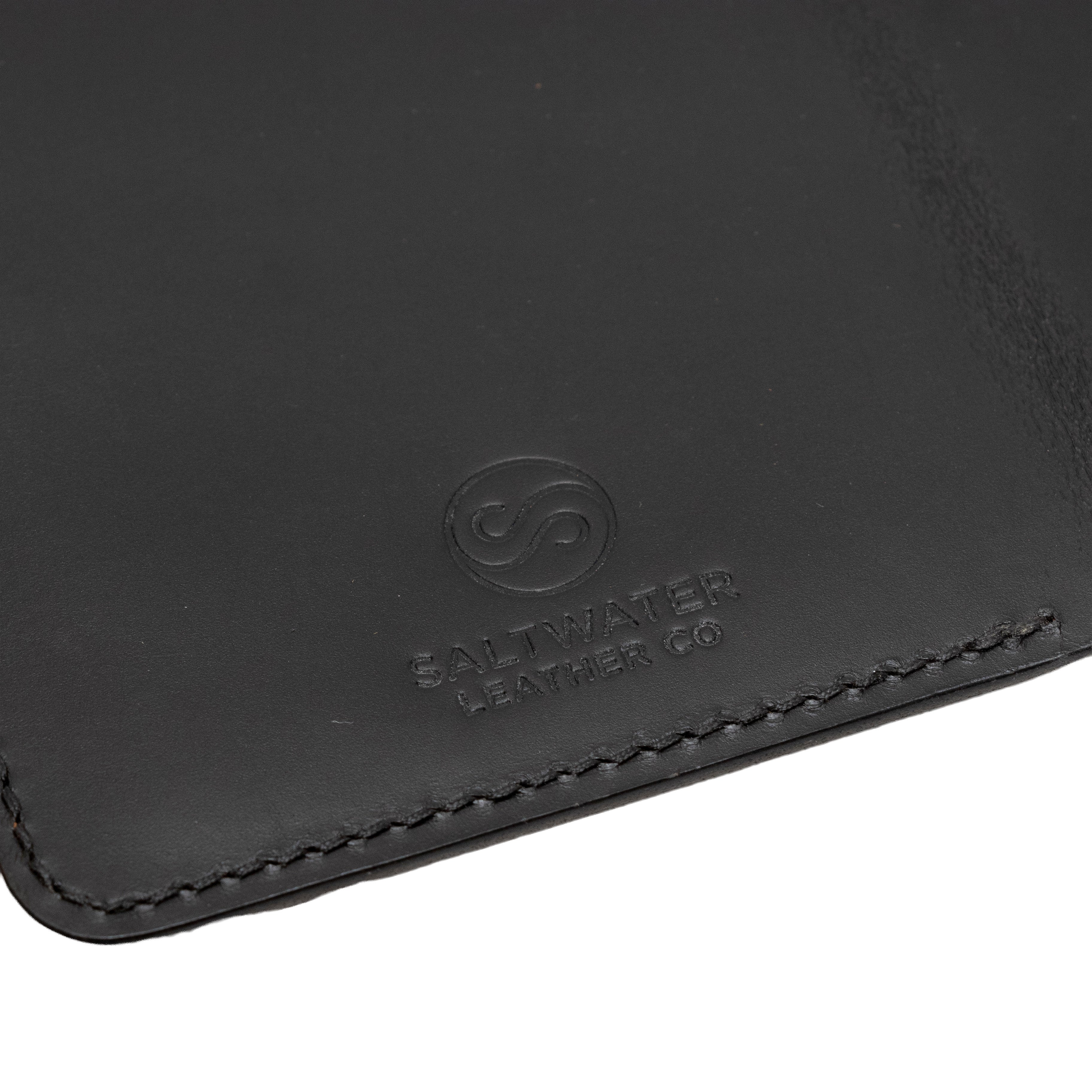 Close-up of a black leather passport holder with Saltwater Leather branding.