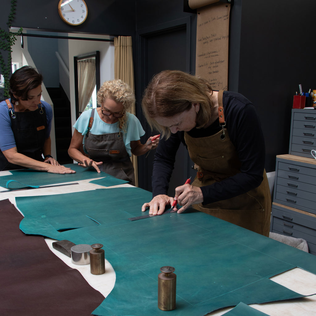Three people working on leather projects in a workshop setting.