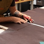 Person cutting brown leather with a red tool on a workbench.