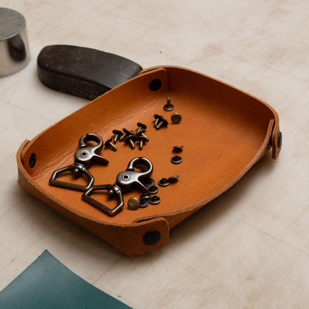 Brown leather tray with metal clips and screws on a beige surface