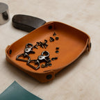 Brown leather tray with metal clips and screws on a beige surface