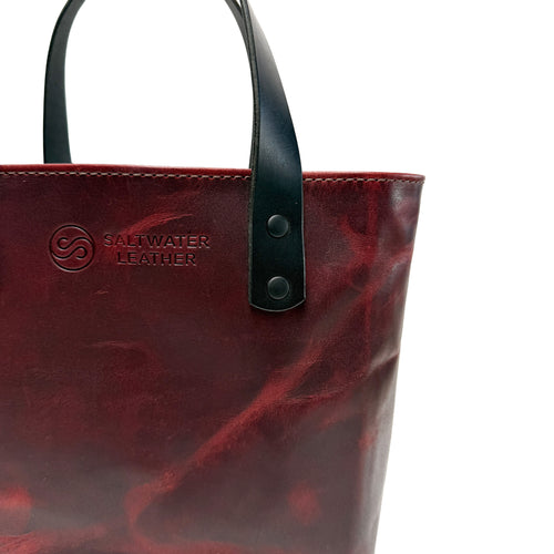 Red leather tote bag with black handle on a white background