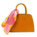 Orange handbag with a colorful floral scarf draped over it on a white background