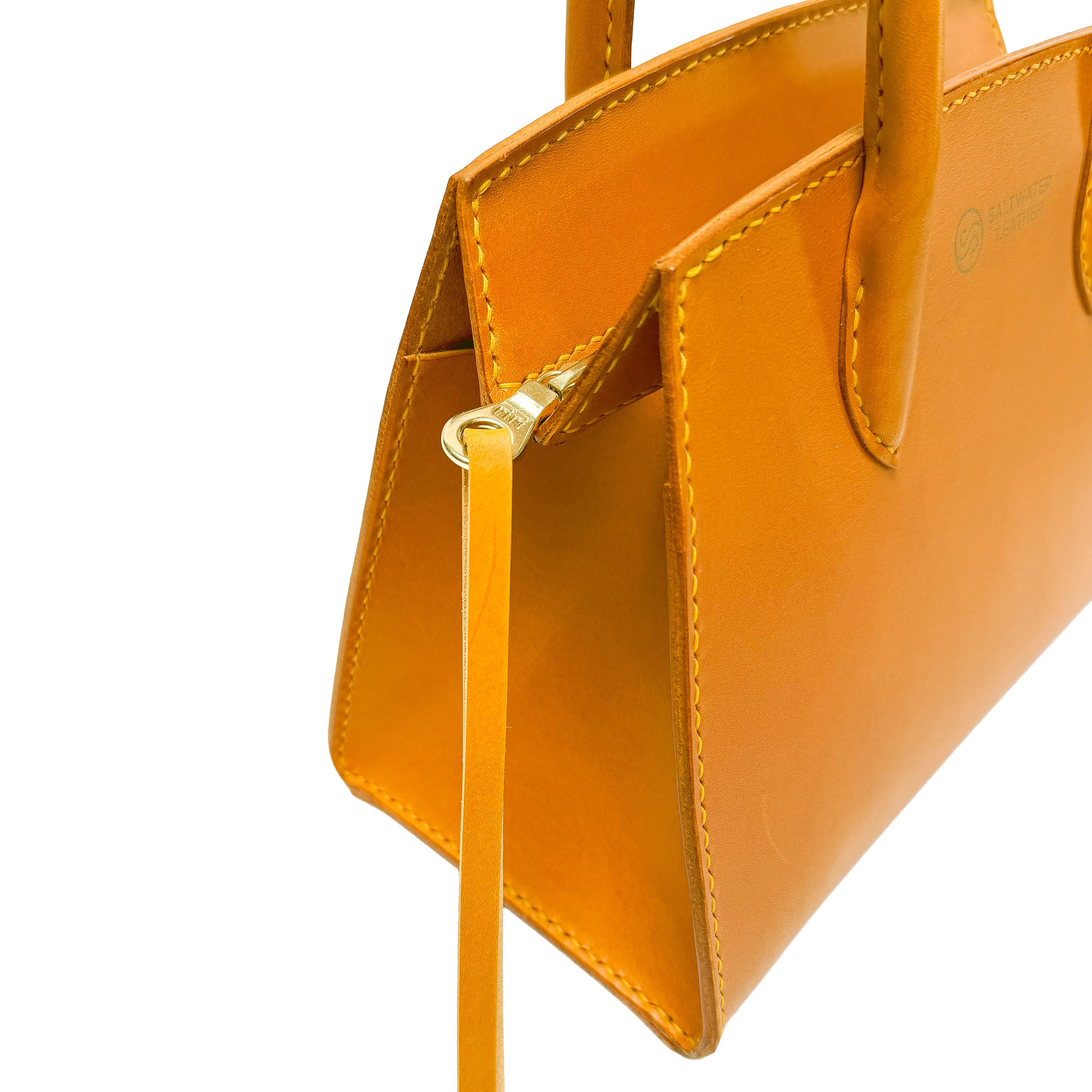 Close-up of a mustard yellow handbag with a visible brand logo on a white background