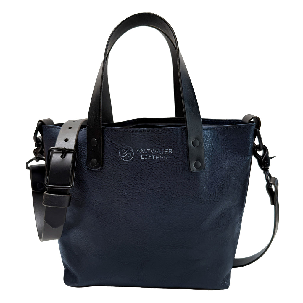 Navy leather handbag with black straps on a white background, featuring the Saltwater Leather logo.