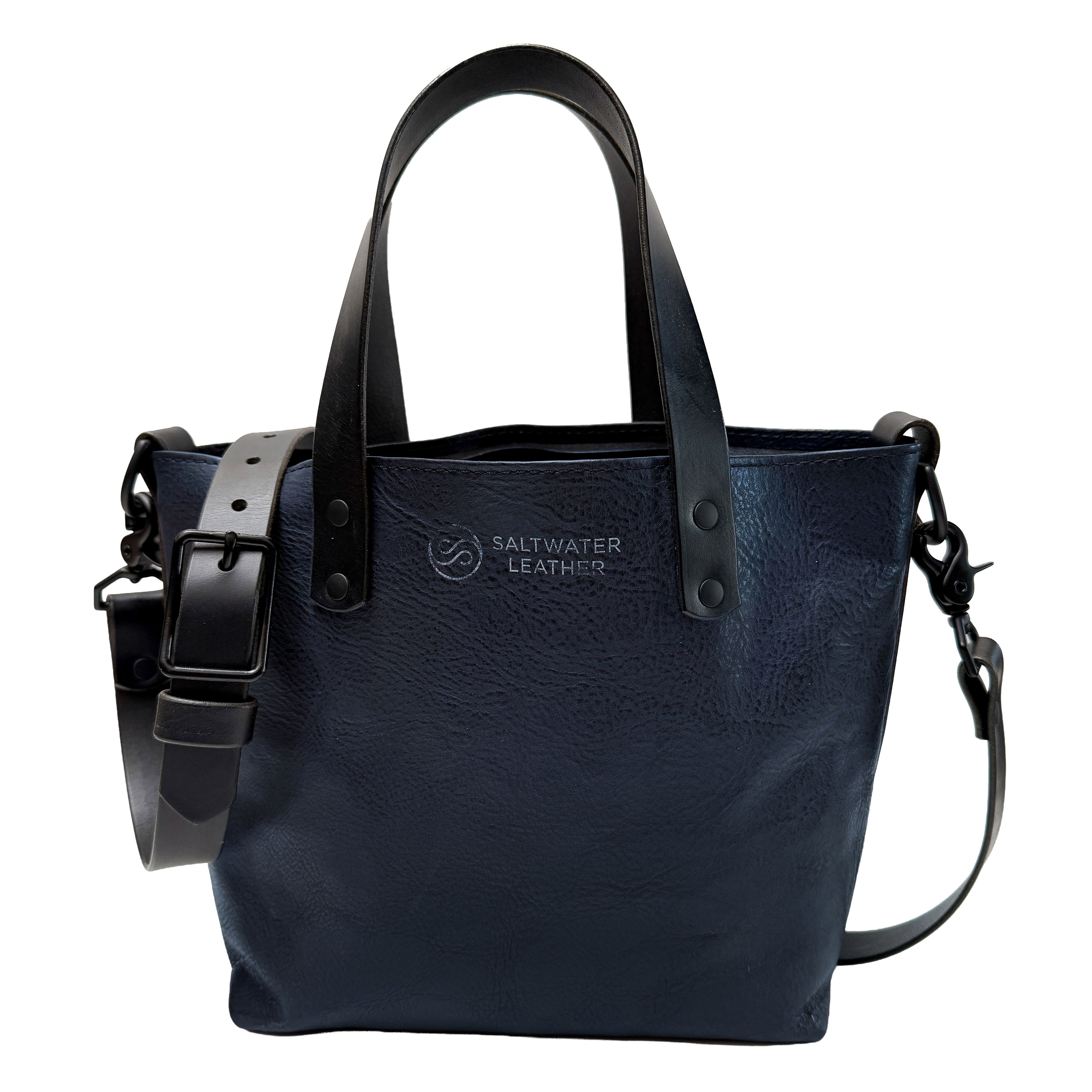 Navy leather handbag with black straps on a white background, featuring the Saltwater Leather logo.