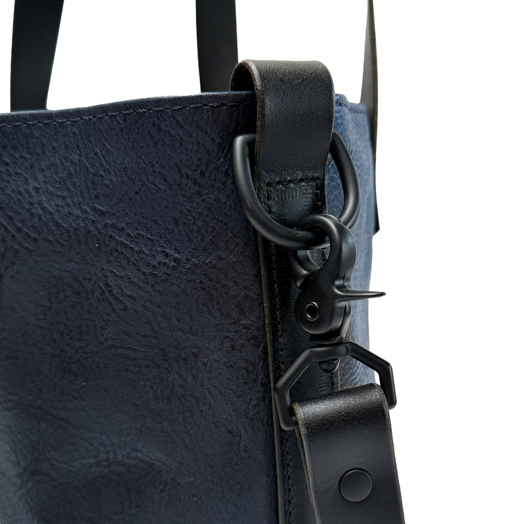Close-up of a navy blue leather bag with black strap and hardware on a white background