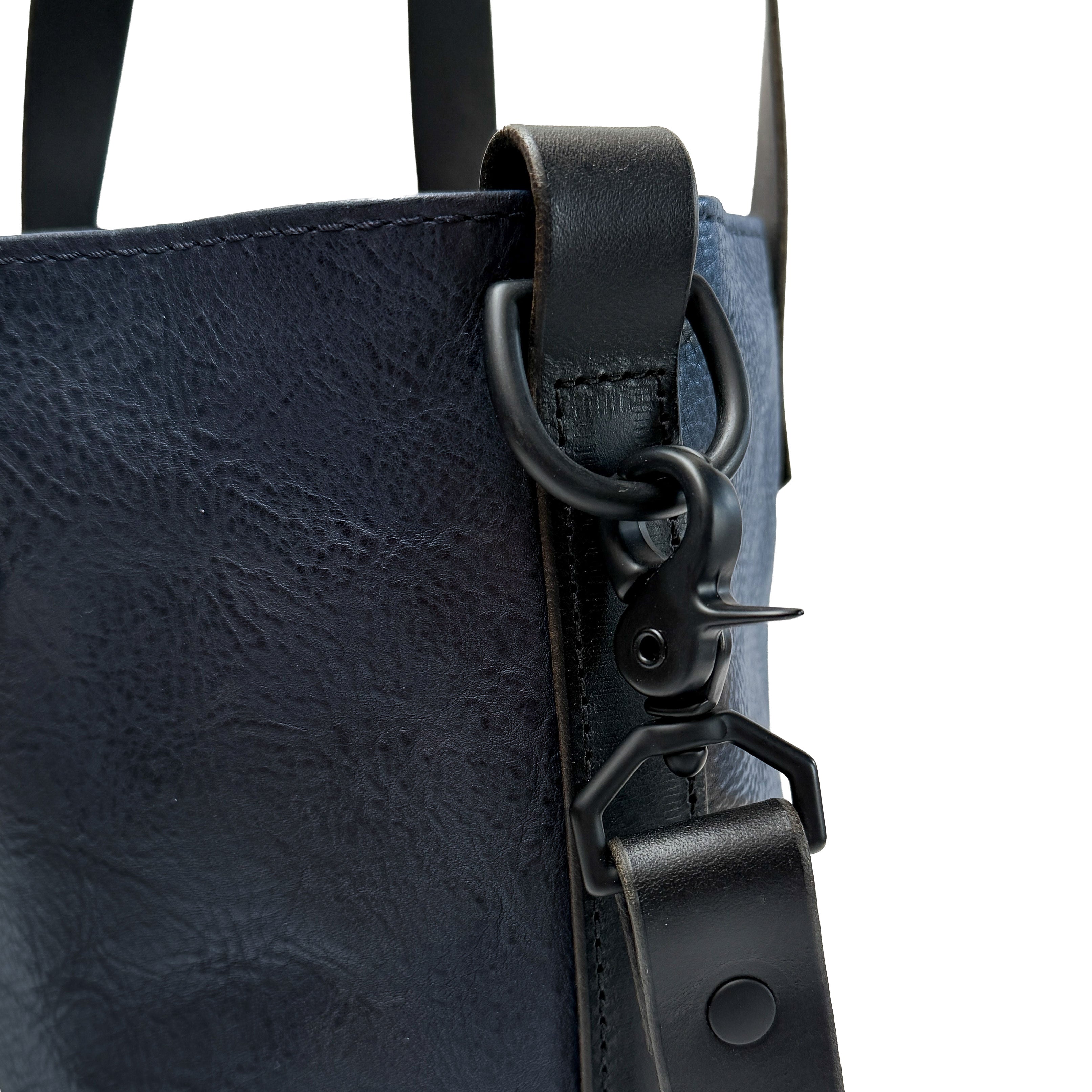 Close-up of a navy blue leather bag with black strap and hardware on a white background
