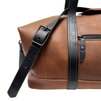 Brown leather duffle bag with black strap on a white background