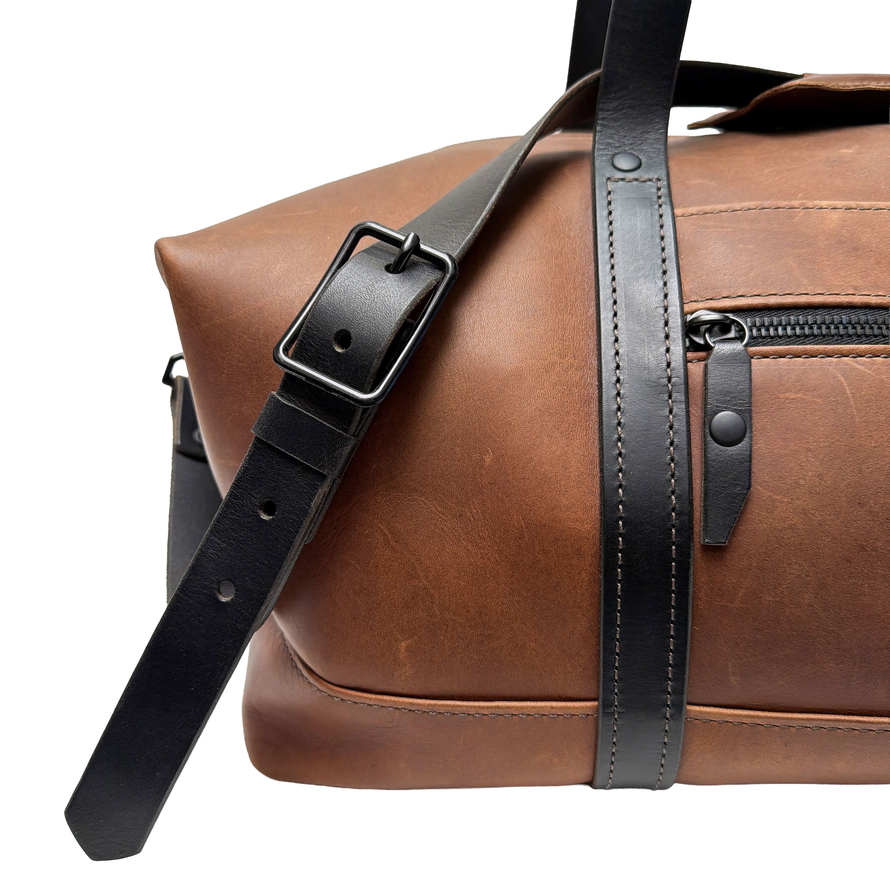 Brown leather duffle bag with black strap on a white background