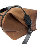 Brown leather duffle bag with black strap on a white background