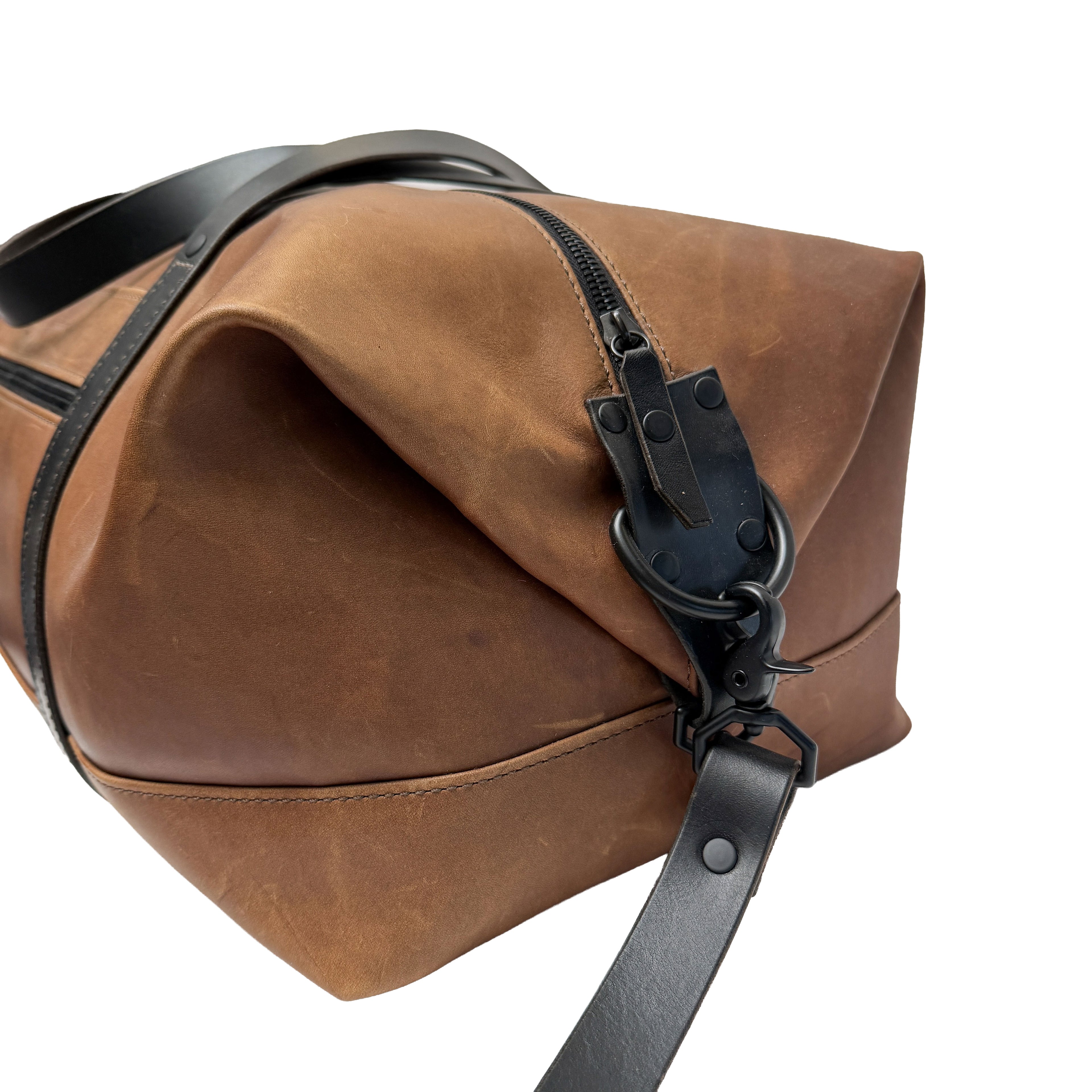 Brown leather duffle bag with black strap on a white background