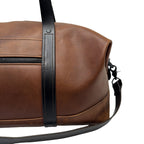Brown leather duffle bag with black strap on a white background