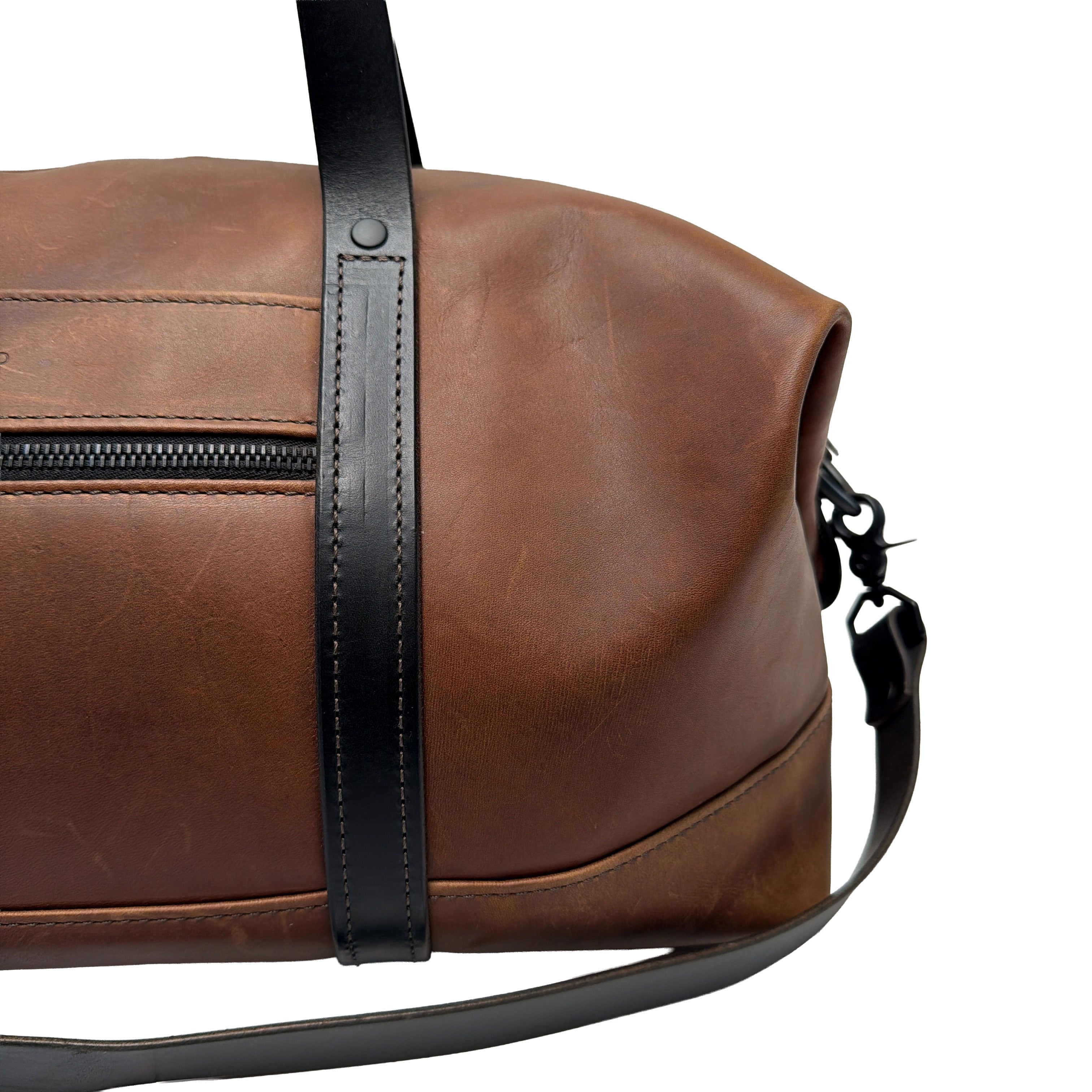 Brown leather duffle bag with black strap on a white background