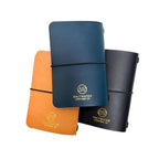 Three Saltwater Leather journal covers in Pacific blue, Mustard yellow, and Midnight black, stacked together against a white background with gold foil logo embossing and elastic band closures.