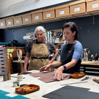 Two women working together in a workshop with tools and materials on a table.